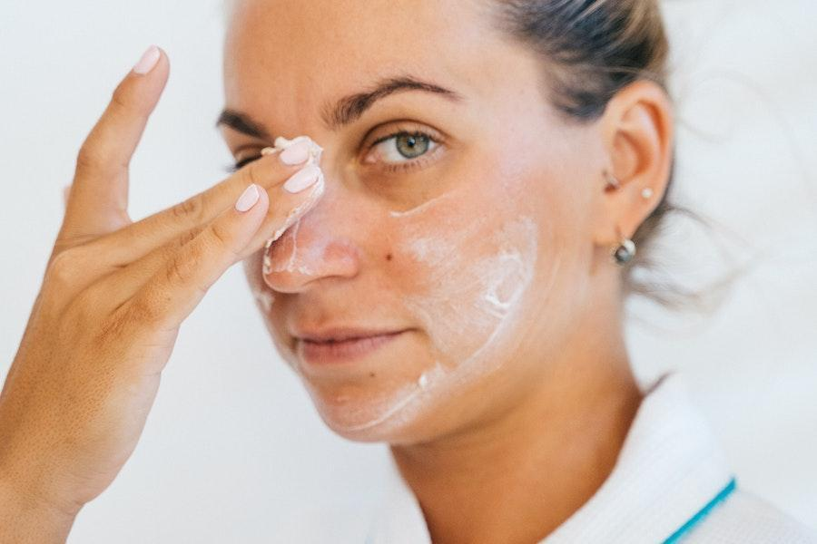 Mujer aplicándose crema facial en la cara