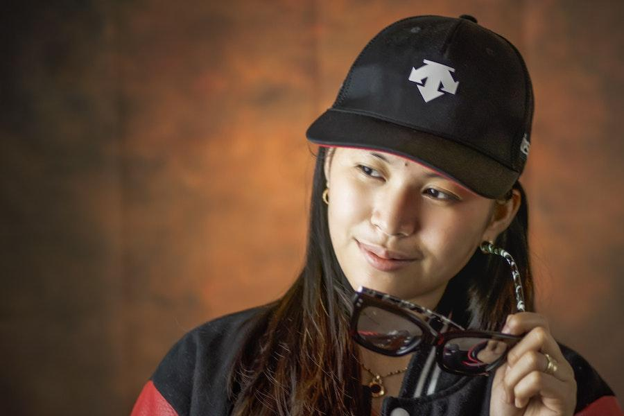 Woman holding glasses while wearing a black baseball cap