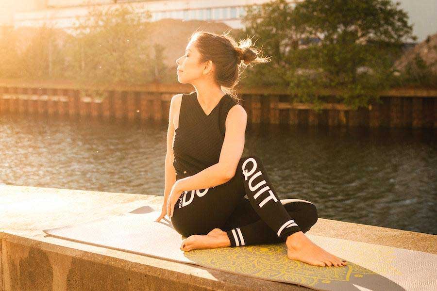 Femme en tenue entièrement noire assise sur un tapis de yoga