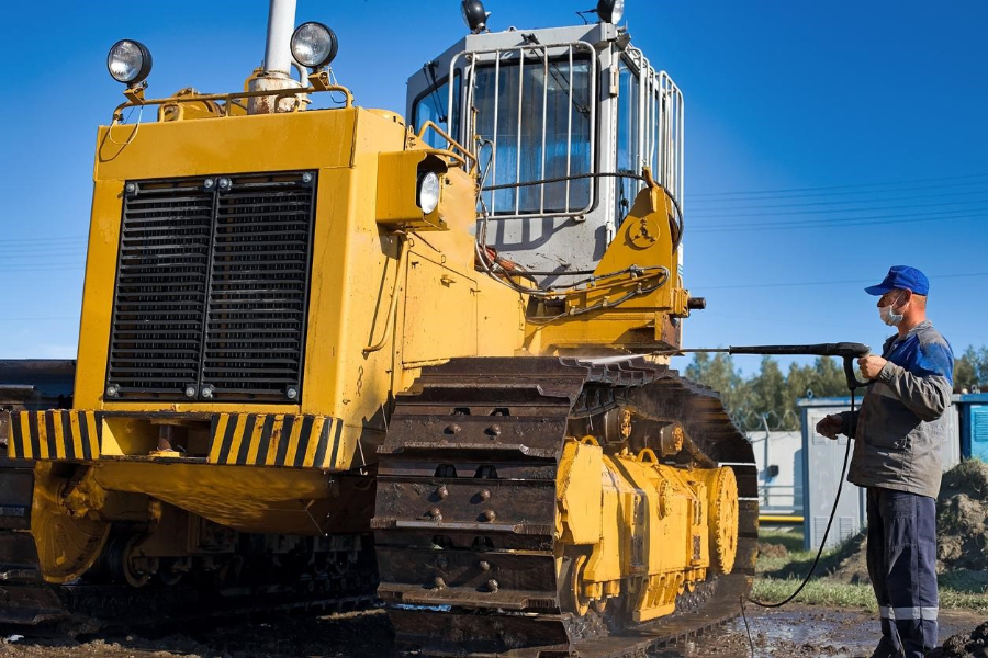 A man washing a yellow crawler tractor