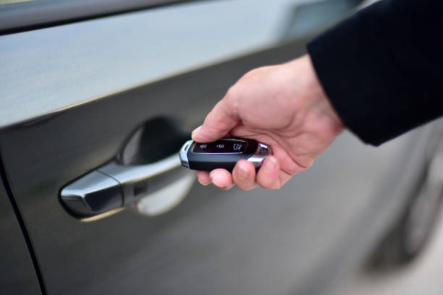 Chiave dell'auto telecomandata in mano accanto alla maniglia dell'auto