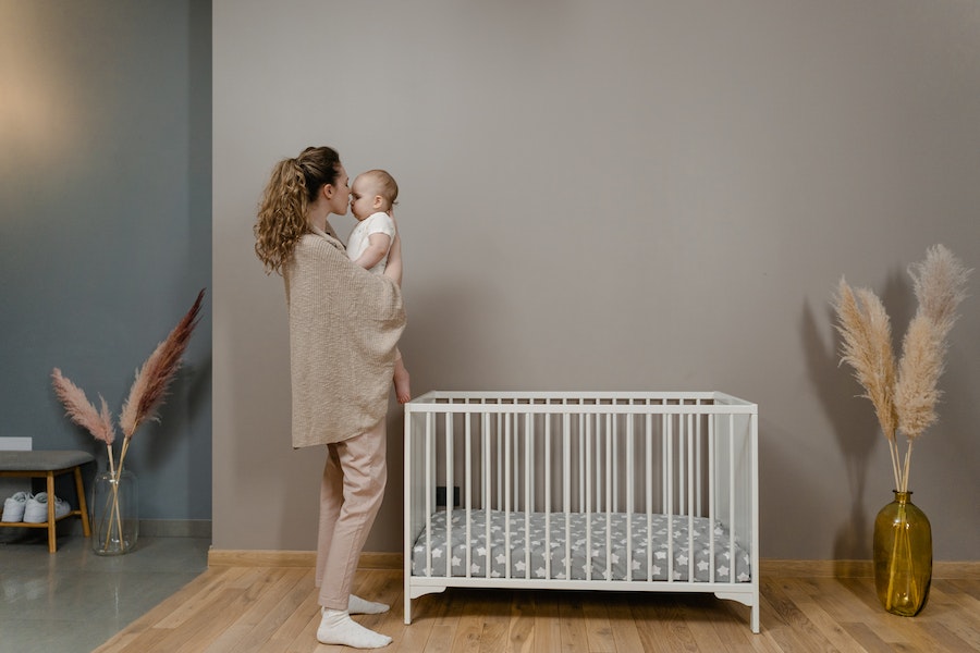 Frau trägt ihr neugeborenes Baby neben einem Kinderbett